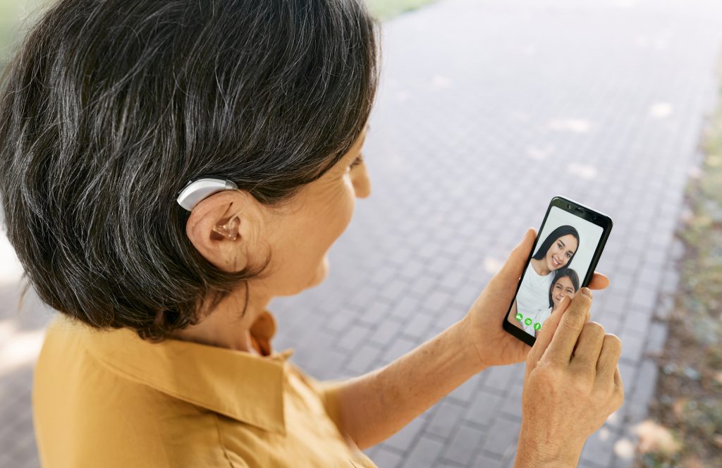 Senior woman with a hearing aid behind the ear communicates with her daughter and granddaughter via video communication via a smartphone.