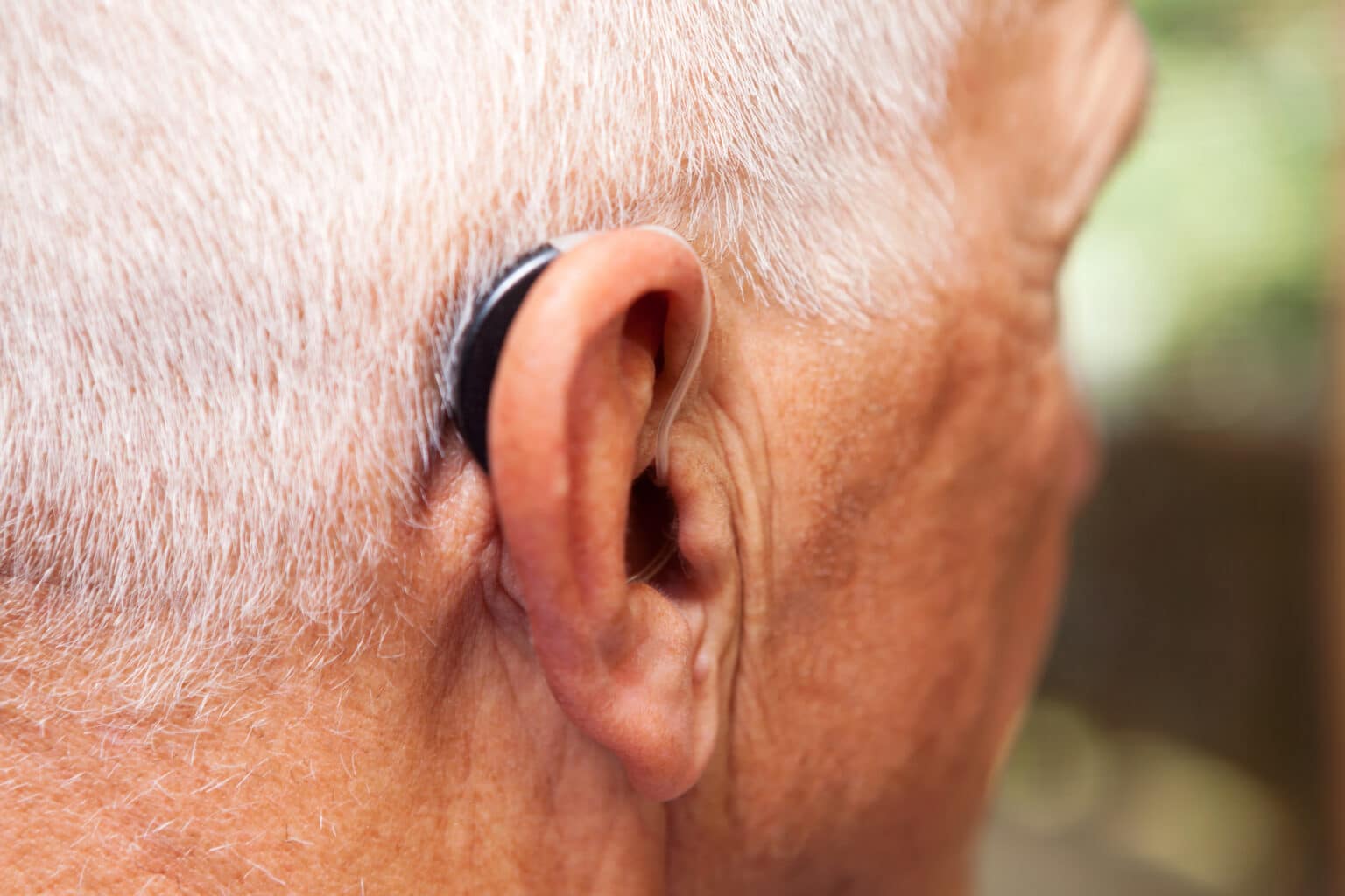 Close up of an older man wearing a behind-the-ear hearing aid.