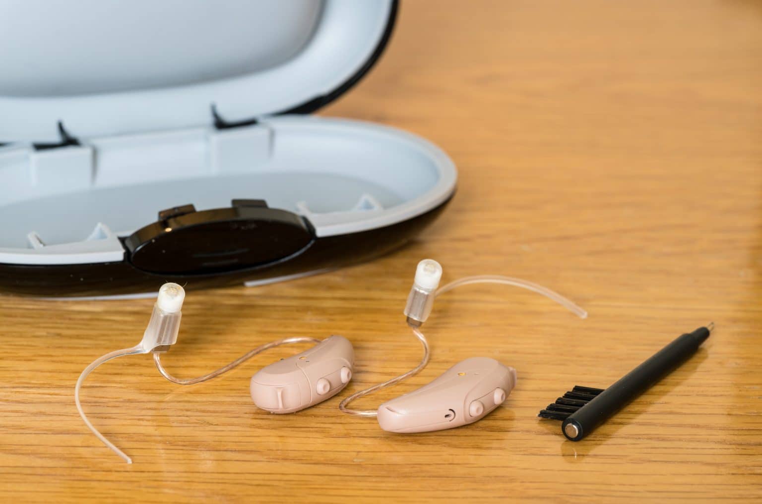 Close up of a pair of hearing aids along with a cleaning brush and case.
