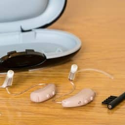 Close up of a pair of hearing aids along with a cleaning brush and case.