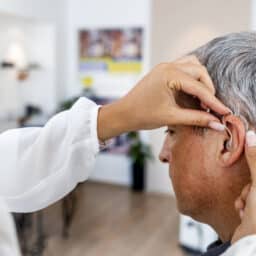 Audiologist putting a hearing aid on a man at the clinic