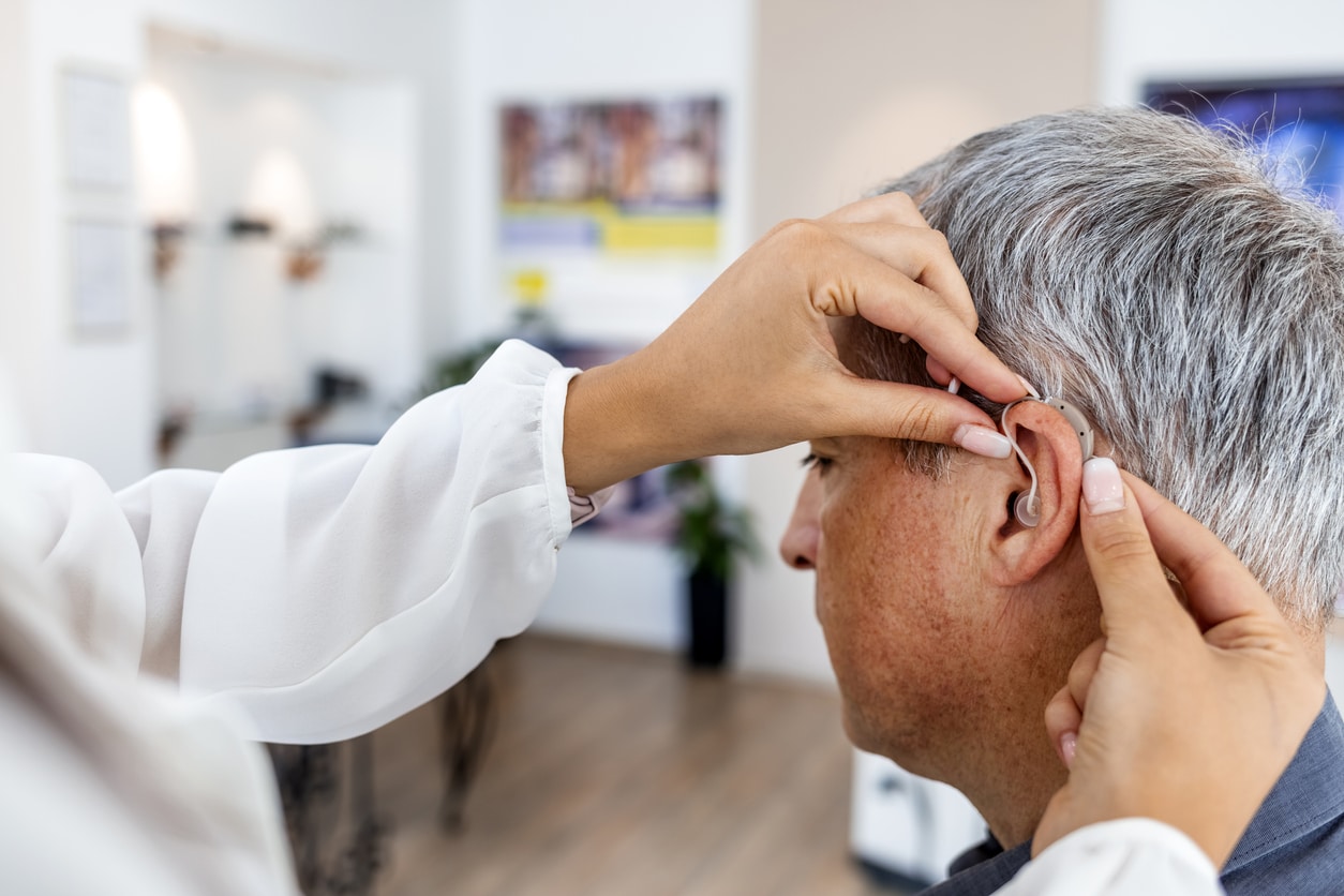 Audiologist putting a hearing aid on a man at the clinic
