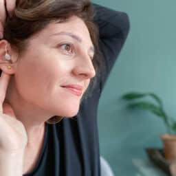 Woman places hearing aid behind ear