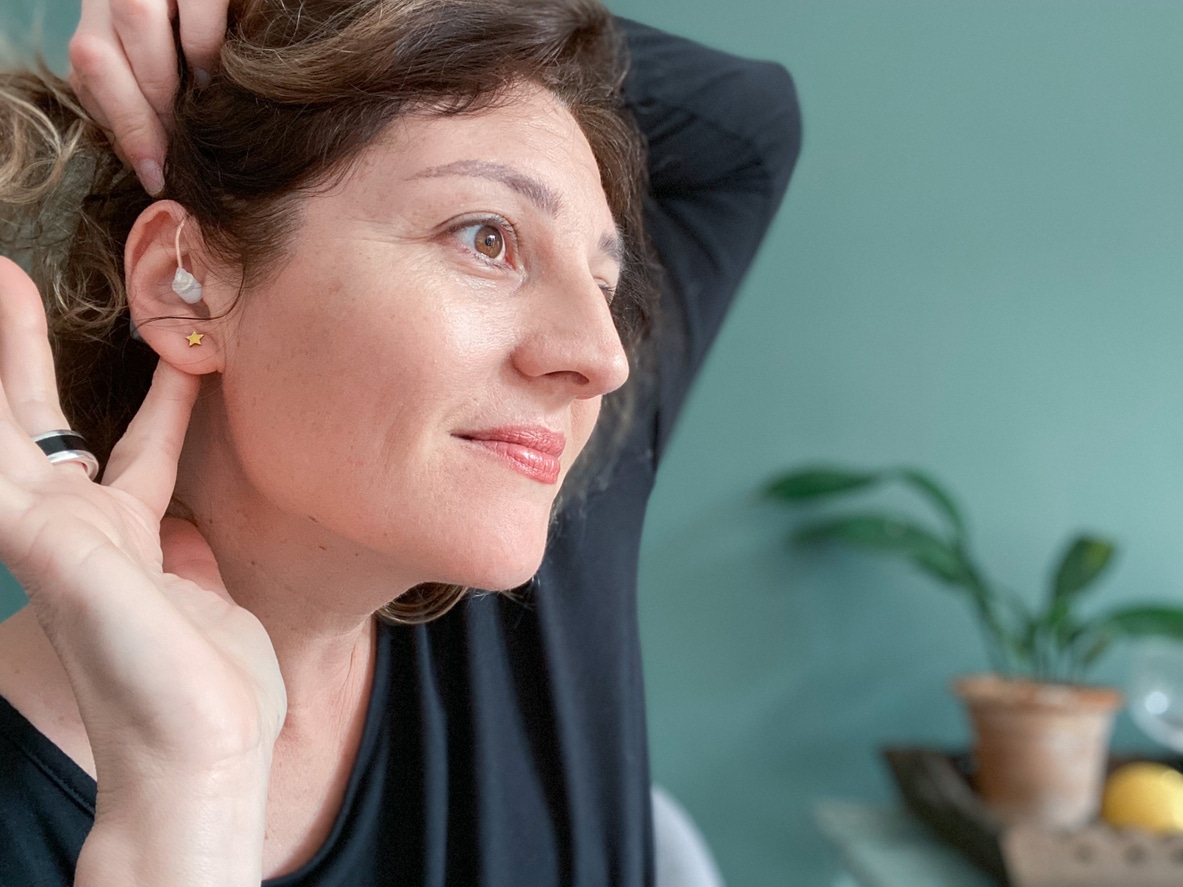 Woman places hearing aid behind ear 