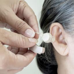 Close up of hands put the hearing aid on the senior woman ear. The device increases louder sounds and then sends them to the ear through a speaker. Caregiver visit. Home health care and nursing home