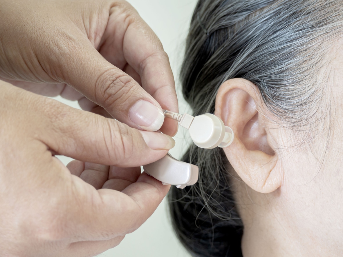 Close up of hands put the hearing aid on the senior woman ear. The device increases louder sounds and then sends them to the ear through a speaker. Caregiver visit. Home health care and nursing home