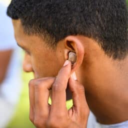 A person wearing hearing aids adjusts the settings using the buttons on the device in their ear.
