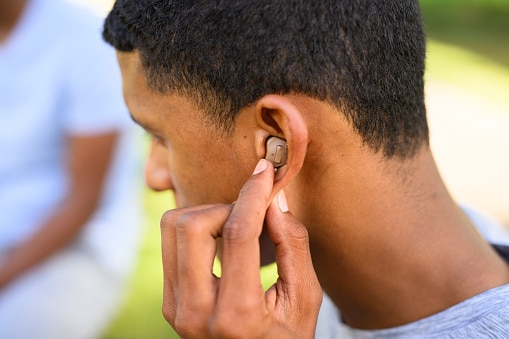 A person wearing hearing aids adjusts the settings using the buttons on the device in their ear.